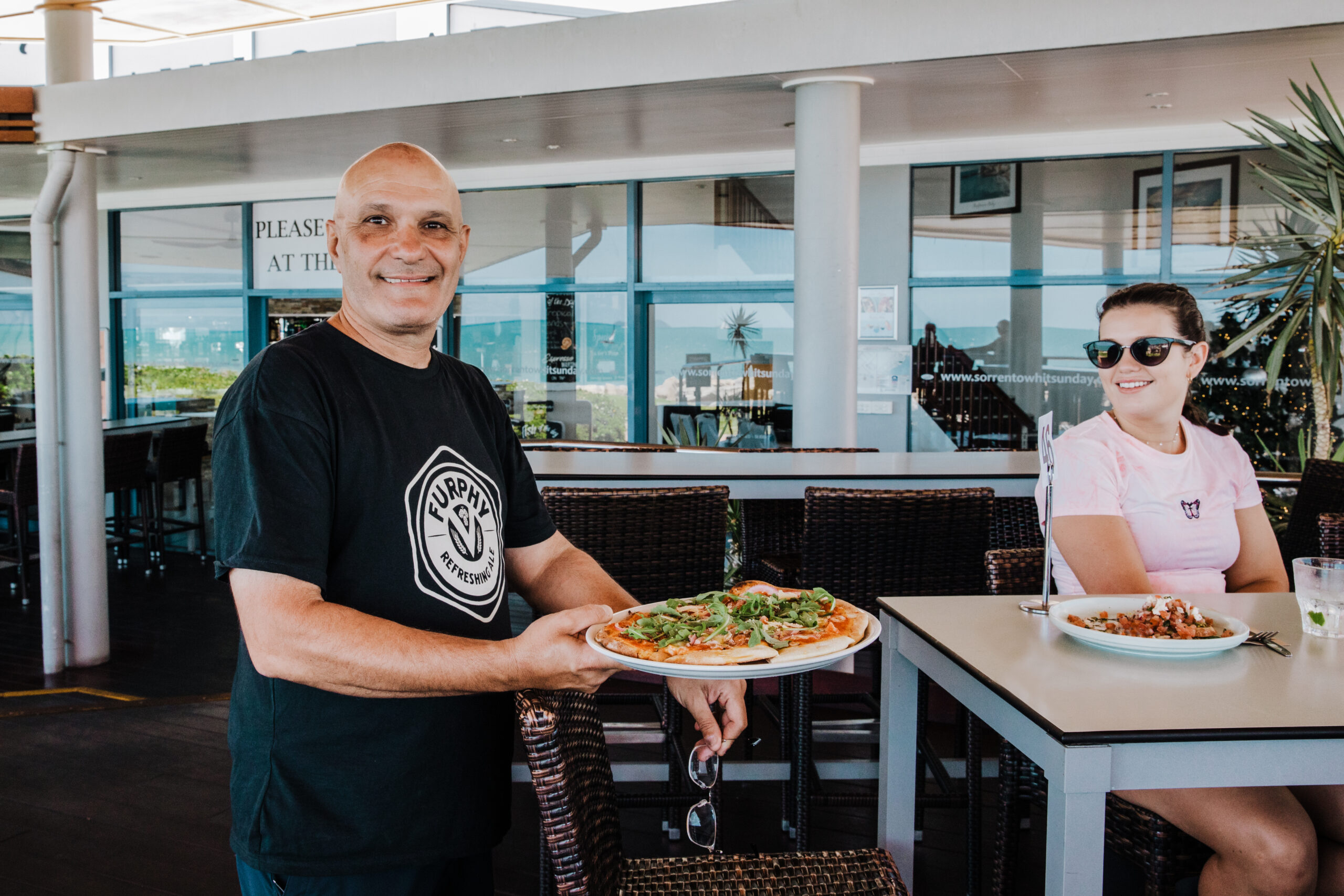 Iyo serving a pizza a man smiling and serving a pizza to the table