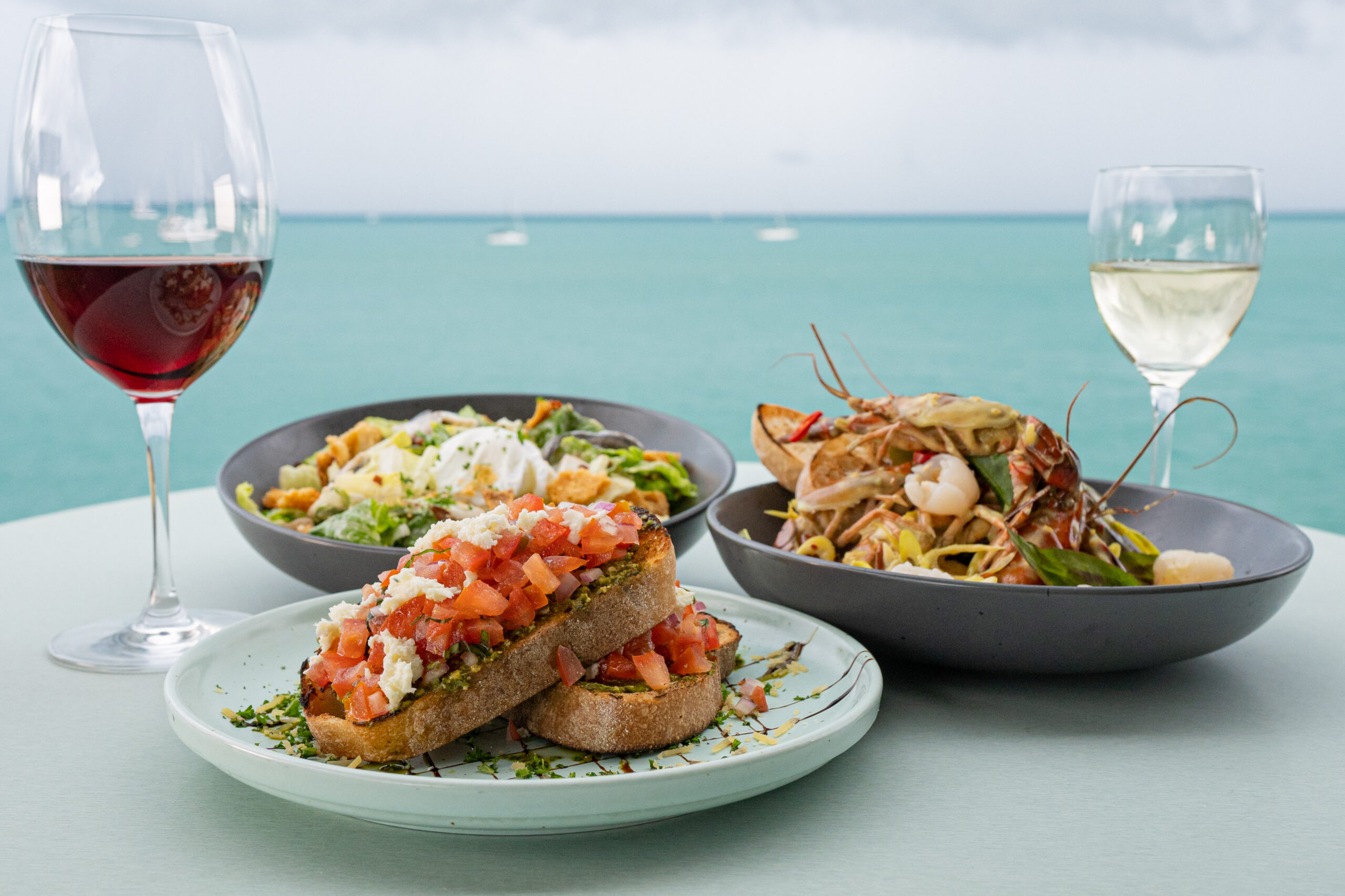 3 dishes and 2 glasses of wine on a table with an ocean view